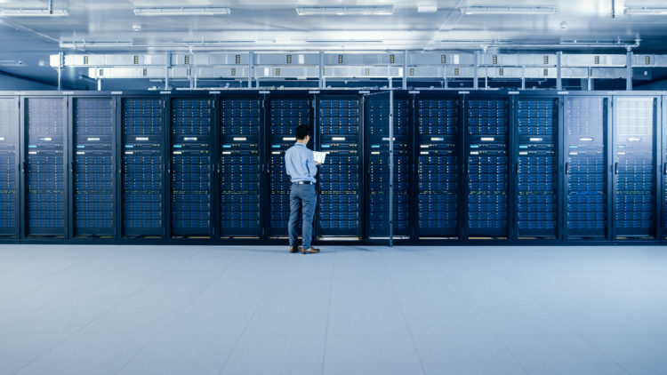 In the Modern Data Center: IT Engineer Standing Beside Open Server Rack Cabinets, Does Wireless Maintenance and Diagnostics Procedure with a Laptop.